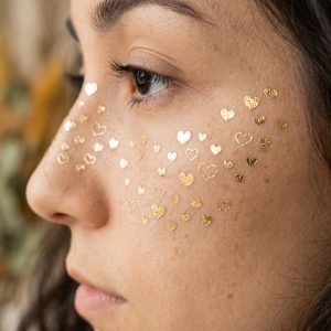 Tiny heart and star temporary tattoos shown on the cheek from a side view