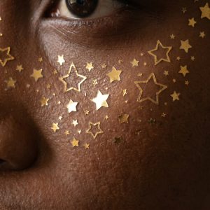 Close-up of tiny metallic star face temporary tattoos on the cheek