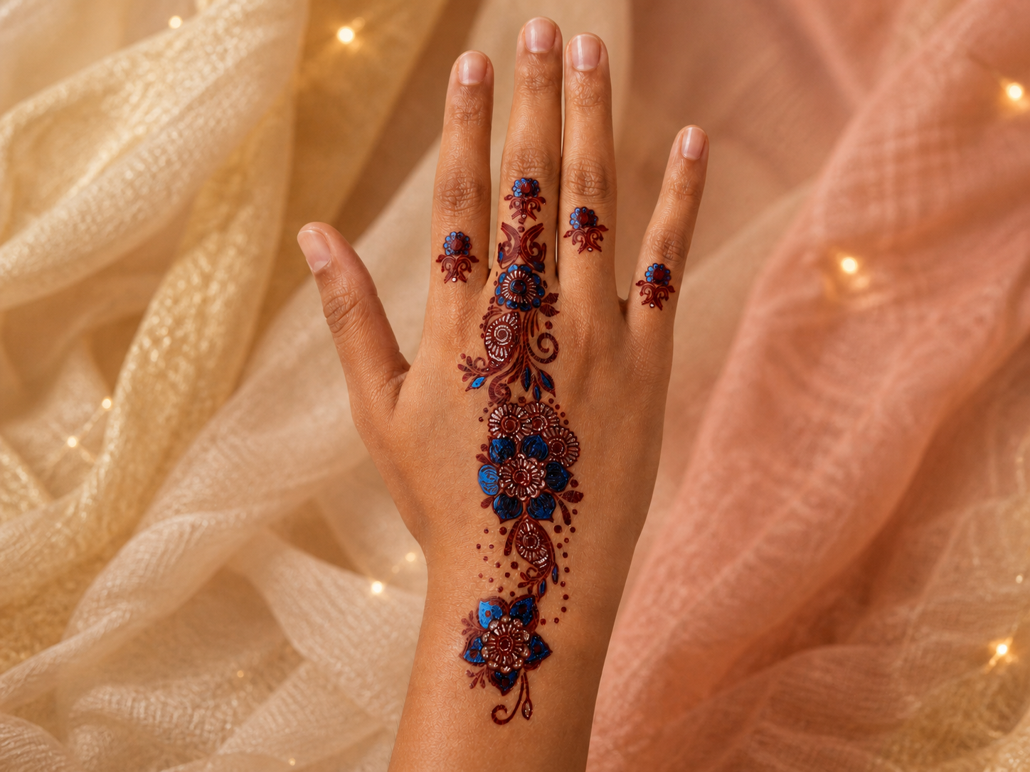 Top view of a hand wearing an ornate blue, burgundy, and metallic floral festival body-art design against draped fabric